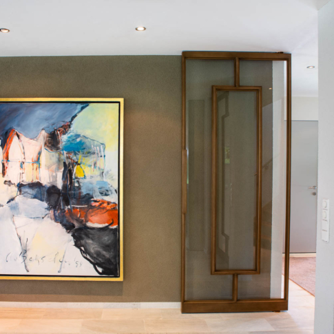 Moderne bronzen stalen binnendeur met glas, naast een groot kunstwerk in een stijlvol interieur.
